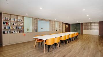 Une salle de conférence dotée d’une longue table, de chaises orange, d’un plancher en bois et d’étagères intégrées.