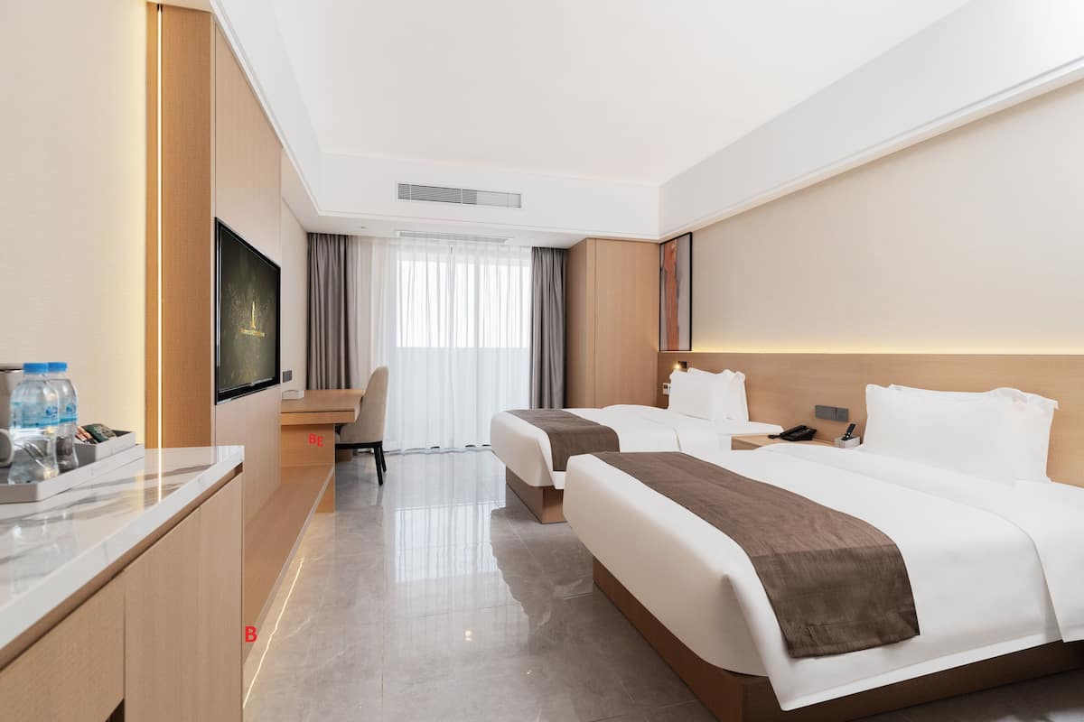 A hotel room with two beds, a desk, a chair, a TV, and a window with curtains.
