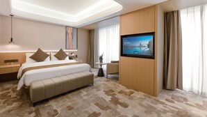 A modern hotel room with a large bed, a flat-screen TV mounted on the wall, a desk with a lamp, and a view of a body of water through the window. - JD POLMAN Hotel (Phnom Penh)