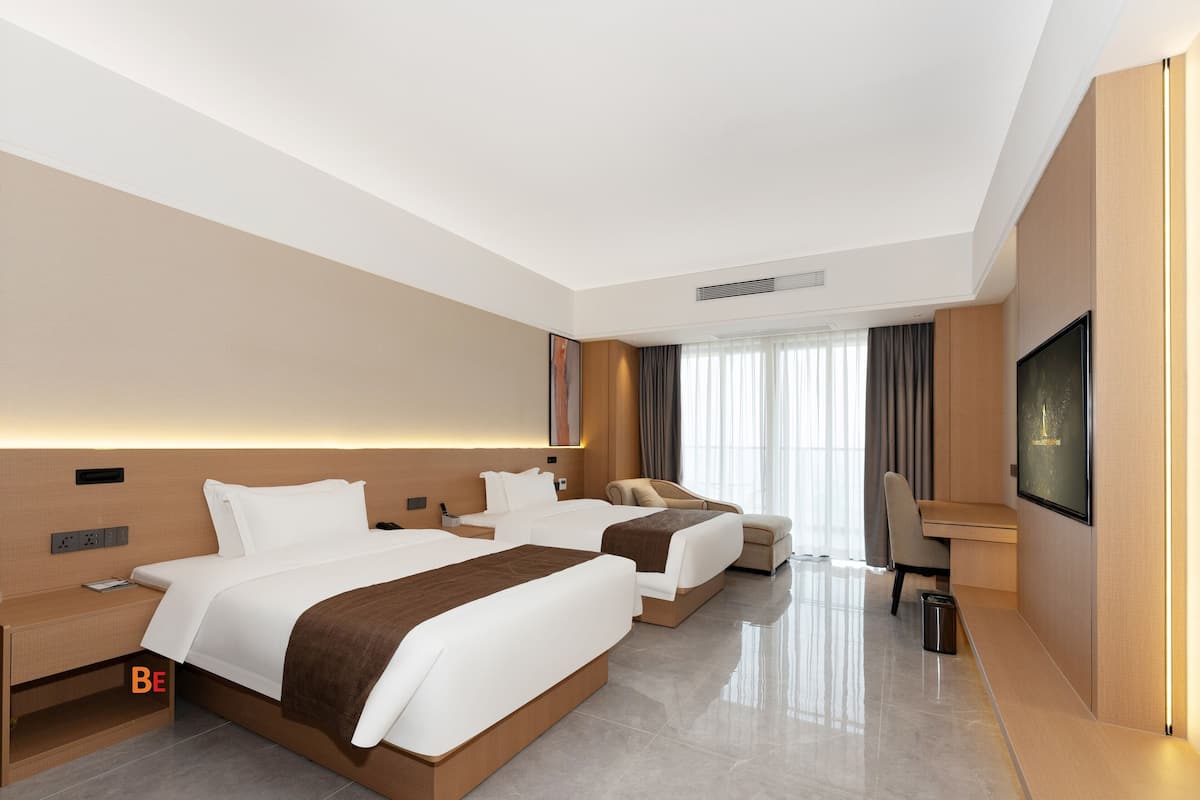 A modern hotel room with two beds, a desk, and a TV.
