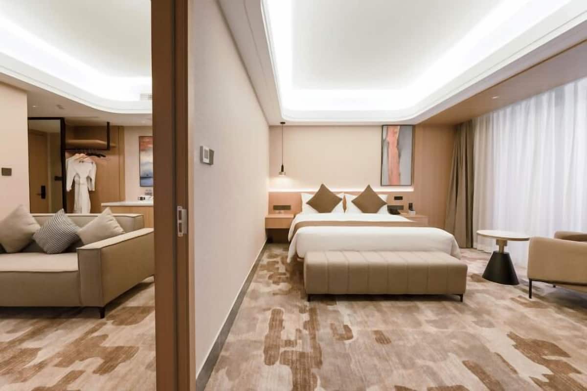 A modern hotel room with a large bed, a sofa, a small table, and a wardrobe.