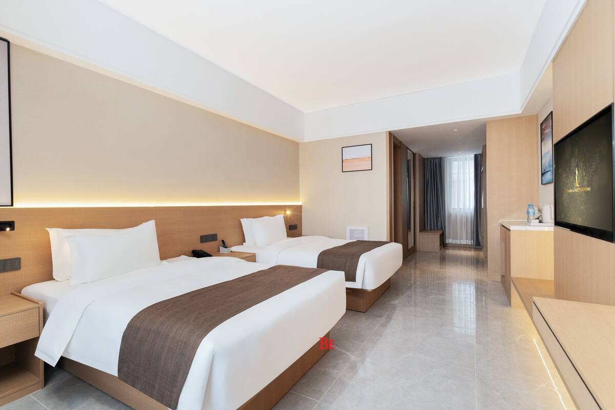 A hotel room with two beds, a flat-screen TV, a desk, and a bathroom visible in the background.