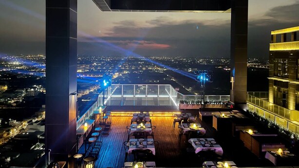 A rooftop dining area with tables and chairs, overlooking a cityscape at dusk. - JD POLMAN Hotel (Phnom Penh)