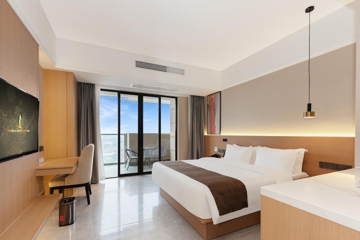 A modern hotel room with a large bed, a desk, a TV, and a balcony with a view.