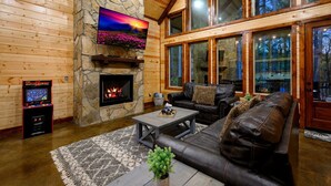 Een houten chalet inrichting met een stenen openhaard, een flatscreen televisie, leren banken en grote ramen.