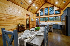 A wooden cabin interior with a dining area, kitchen, and large windows. - Chillax Inn · Tranquil Getaway: Pet-Friendly, Hot Tub & Foosball (Broken Bow)