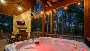 Een hottub in een houten terras met stenen muren, een open haard en een aan de muur bevestigde televisie.