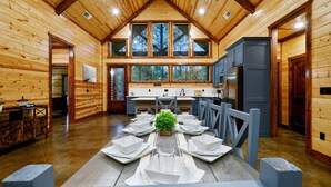 Een houten chalet van binnen met een eethoek voor zes personen, een keuken met een koelkast en grote ramen.