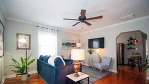 A living room with a blue sofa, a lamp, a ceiling fan, and a dining area with a table and chairs. - Westfield Blue (Richmond)