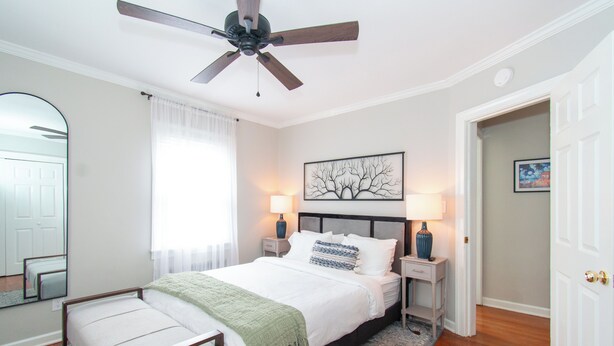 A bedroom with a bed, bedside tables, a ceiling fan, a mirror, and a door. - Westfield Blue (Richmond)