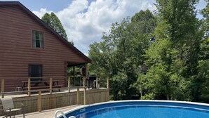 Una terraza de madera con piscina, mesa de picnic y zona de estar cubierta.