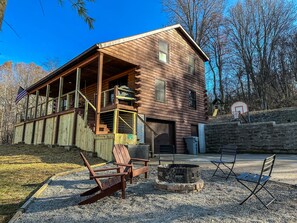 Eine Blockhütte mit Veranda, Feuerstelle und Gartenmöbeln.