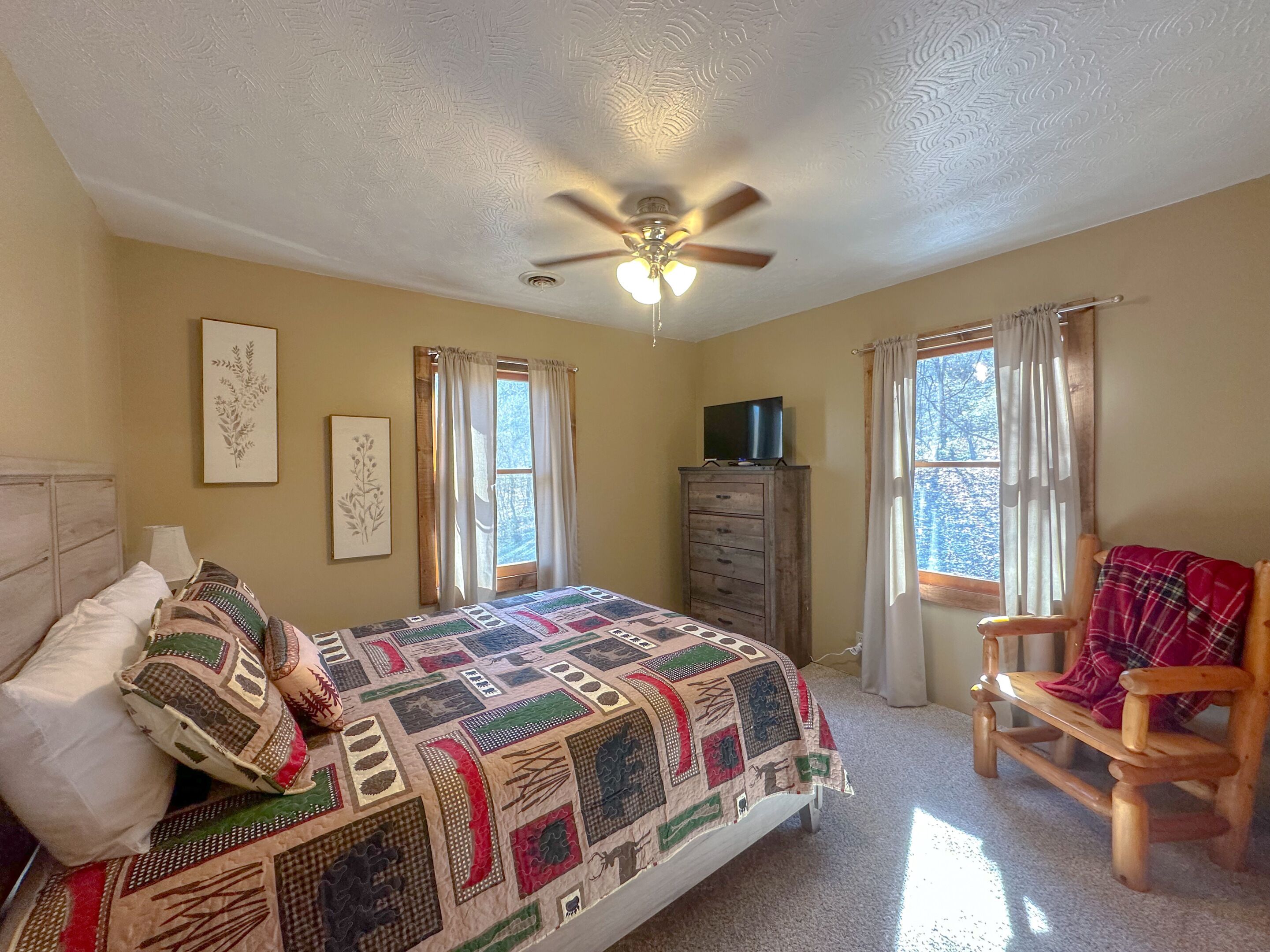 A bedroom with a bed, a wooden dresser, a chair, and a ceiling fan.