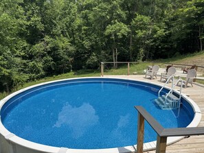 A round swimming pool with a wooden deck and white chairs.