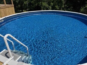 En klar, blå swimmingpool med en træterrasse og en metalstige.