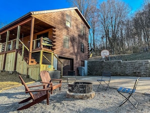 A wooden cabin with a balcony, a basketball hoop, and outdoor seating.