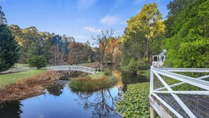 Un parc paisible avec un pont blanc, un étang parsemé de nénuphars et un kiosque.