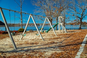 Enjoy swings and a slide on a sandy surface overlooking a serene lake.