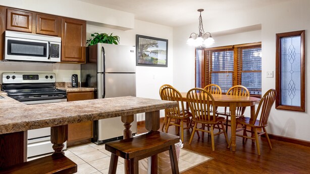 A kitchen with wooden cabinets, a granite countertop, a dining table with chairs, and a refrigerator. - 2 Bedroom Condo in Lakeside Resort Community (1 King & 2 Queen Beds) (DuBois)