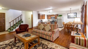 A living room with a sofa, armchair, and coffee table, a staircase, and a kitchen area with cabinets, microwave, and refrigerator. - 2 Bedroom Condo in Lakeside Resort Community (1 King & 2 Queen Beds) (DuBois)