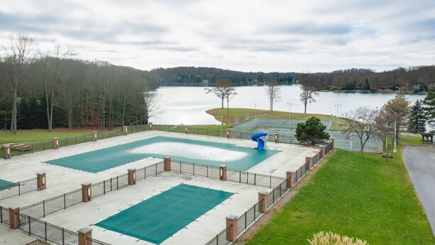 Una gran piscina al aire libre con un deck circundante y bancos, con vistas a un lago y colinas boscosas.