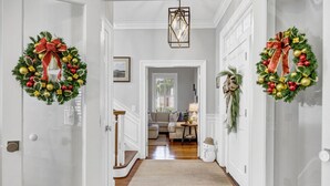 Ein Flur mit zwei Türen, geschmückt mit Weihnachtskränzen, einer Treppe, einem Wohnzimmer mit Sofa und Lampe sowie einer Schneemandel-Deko.