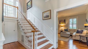 Eine Treppe mit weißen Geländern und Holzstufen führt zu einem Wohnbereich mit einer Couch und einer Lampe.