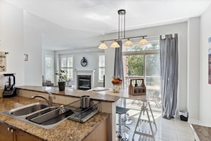 A modern kitchen with a granite countertop, stainless steel sink, and a fireplace.