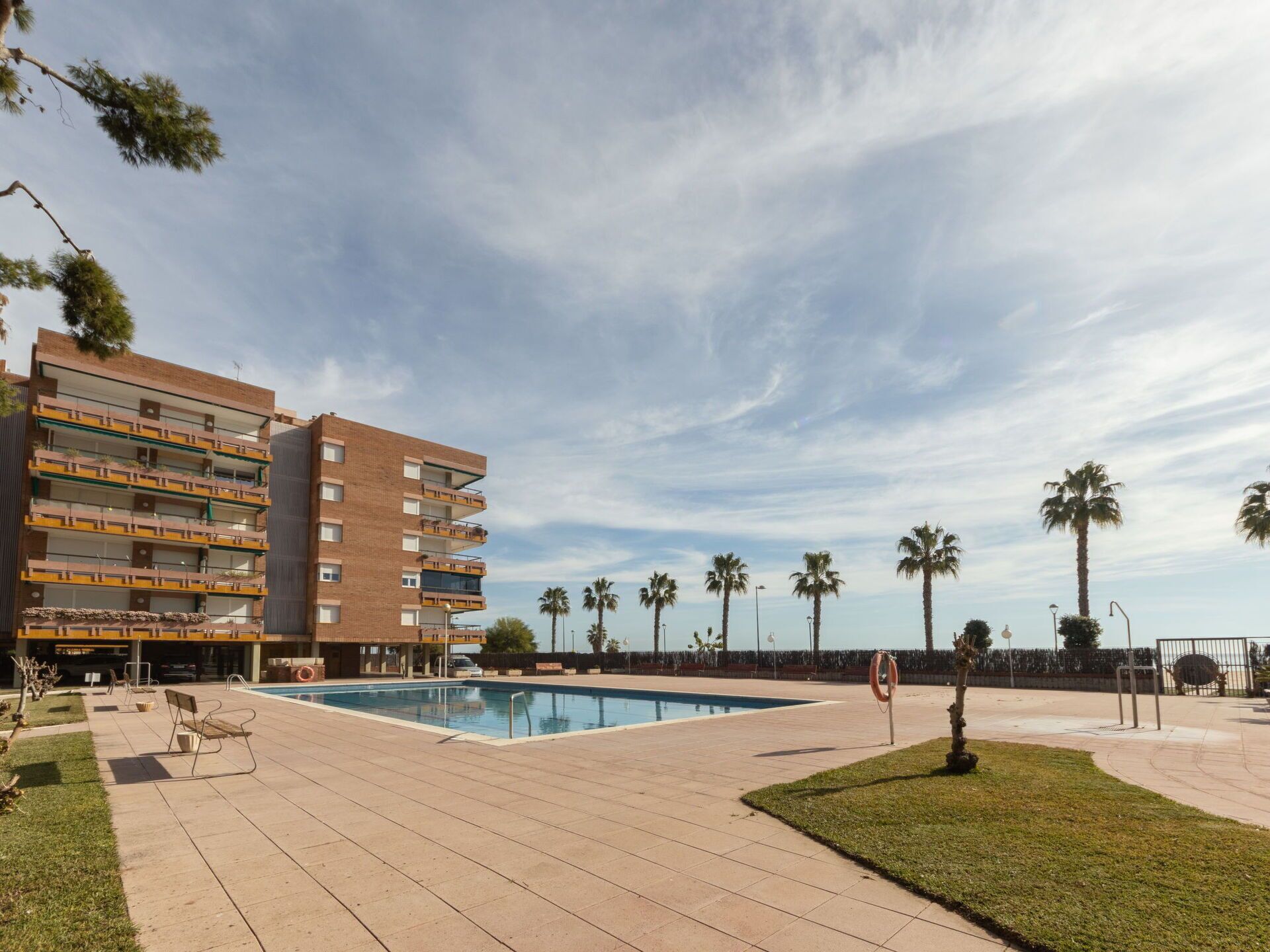 A multi-story hotel with a swimming pool, palm trees, and a clear sky.