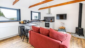 A modern kitchen with a central island, a built-in oven, and a black stove. There is a red sofa and a wooden ceiling. - The Cabin in the Tamar Valley Cornwall (Gunnislake)