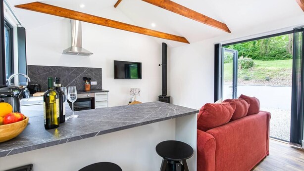 A modern kitchen with a marble countertop, a built-in stove, and a large window offering a view of the outdoors. - The Cabin in the Tamar Valley Cornwall (Gunnislake)