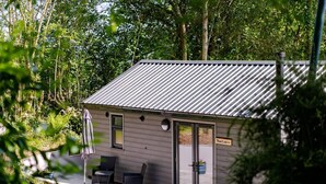 A cabin with a metal roof, two windows, and a door. There is a sign that reads "The Cabin" and a small outdoor seating area with a table and chairs. - The Cabin in the Tamar Valley Cornwall (Gunnislake)