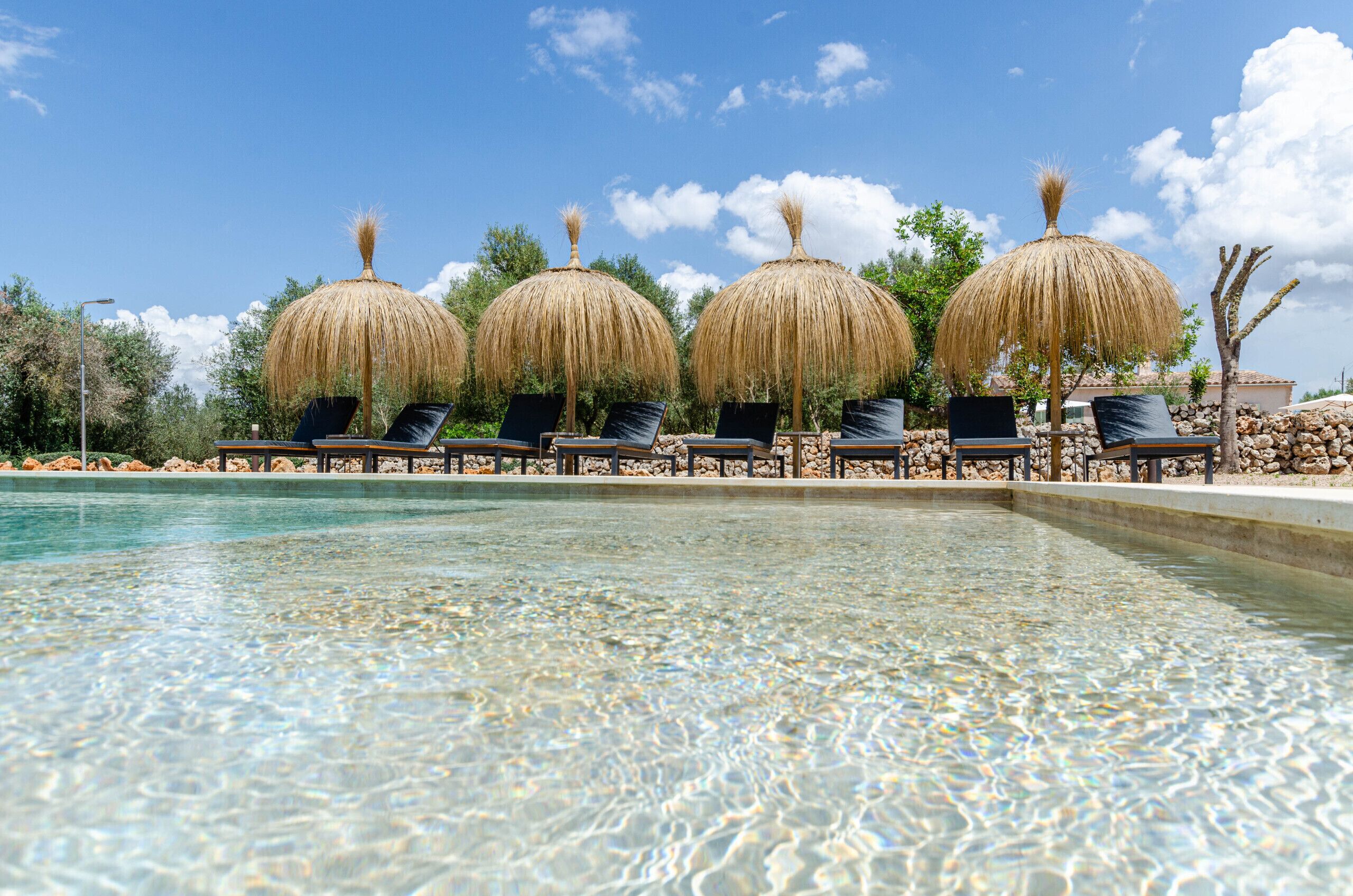 A pool with clear water, surrounded by lounge chairs and thatched umbrellas.