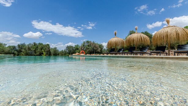 Piscina nítida en un ambient tropical, amb sombrerets de palla i gandules.