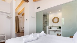 Habitació d'hotel moderna amb un llit gran, un bany amb dutxa de vidre i un sostre de fusta.