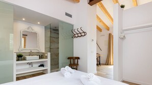 A modern hotel room with a large bed, a bathroom with a mirror and sink, and a wooden ceiling. - Cal Tio 4 YourHouse, lovely apartment in a farmhouse with shared pool (Costitx)