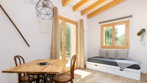 A room with a wooden dining table, chairs, a bed with a window, and a hanging plant. - Cal Tio 4 YourHouse, lovely apartment in a farmhouse with shared pool (Costitx)