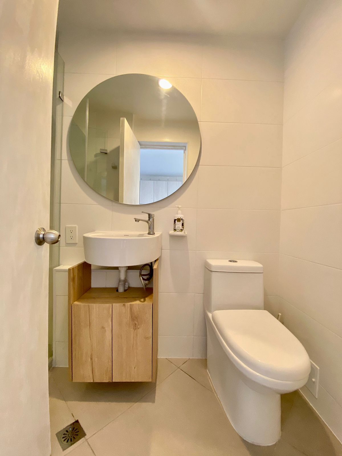 A bathroom with a round mirror, a white sink, a toilet, and a wooden cabinet.