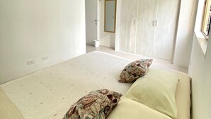Une chambre à coucher au style minimaliste, avec un grand lit, une armoire et une porte donnant sur une autre pièce.
