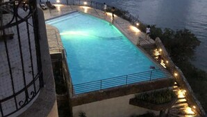 Une piscine bordée de pierres et dotée d’éclairages, offrant une vue sur une étendue d’eau.