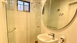 Une salle de bain moderne avec une douche à l’italienne en verre, un meuble-lavabo en bois, un lavabo blanc et un grand miroir.