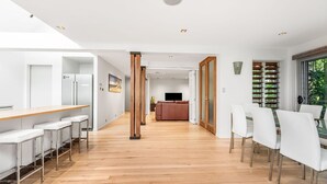 Une cuisine moderne avec un coin bar, un plancher en bois et un espace repas avec des chaises blanches.
