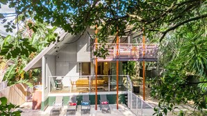 Une maison à deux étages dotée d’un balcon, d’un espace salon extérieur et d’une végétation luxuriante.