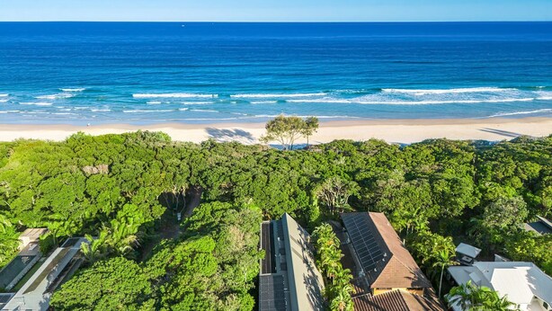 Vue aérienne d’une zone côtière caractérisée par une végétation luxuriante, une plage et des bâtiments équipés de panneaux solaires.