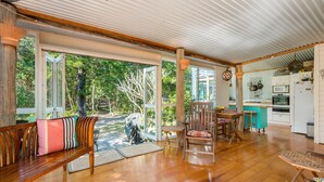 A spacious kitchen with a large island, wooden flooring, and a view of a lush garden through open doors. - Beachcombers Cottage - beachfront pet retreat (Suffolk Park)