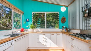 A kitchen with white cabinets, a wooden countertop, a red kettle, and a window with a view of greenery. - Beachcombers Cottage - beachfront pet retreat (Suffolk Park)