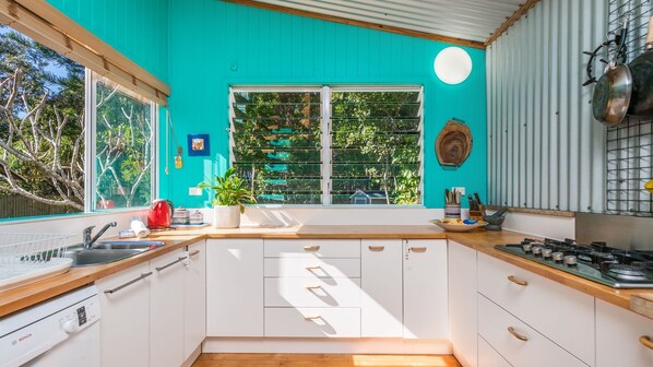 Une cuisine avec des meubles blancs, un plan de travail en bois, une bouilloire rouge et une fenêtre donnant sur un paysage verdoyant.