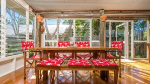 A sunlit dining area with a wooden table and chairs, large windows, and a view of the outdoors. - Beachcombers Cottage - beachfront pet retreat (Suffolk Park)