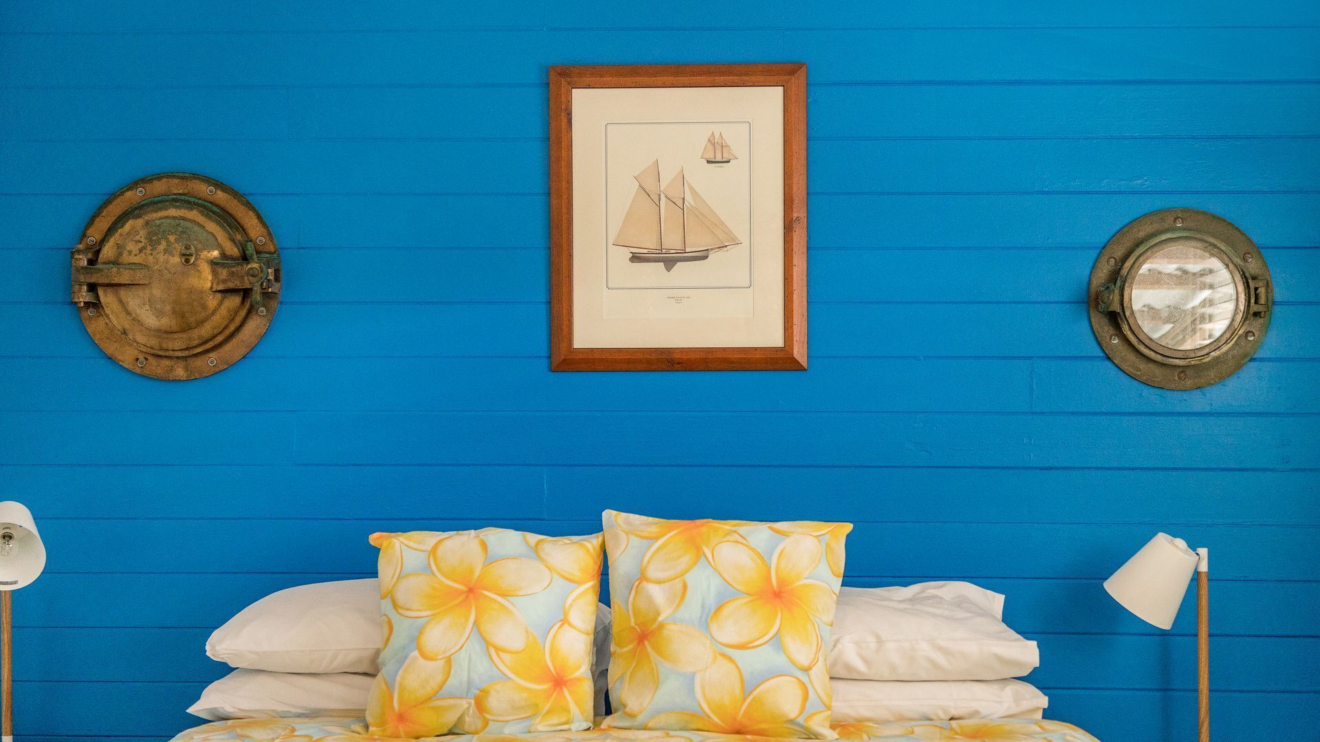 Una habitación con una pared azul, una ilustración enmarcada de un velero y dos objetos metálicos redondos en la pared.