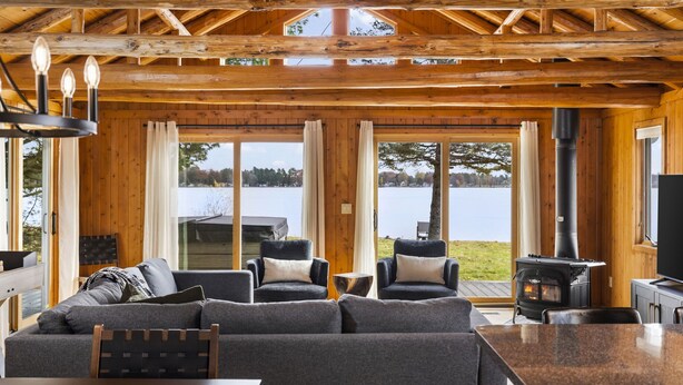 A cozy cabin interior with a large sofa, two armchairs, a dining table, and a wood-burning stove. - ~Fireworks On The 3rd~Sunrise Vista~Lakefront~Dock~Kayaks~Hot Tub~Games~NEW AC~ (Gaylord)